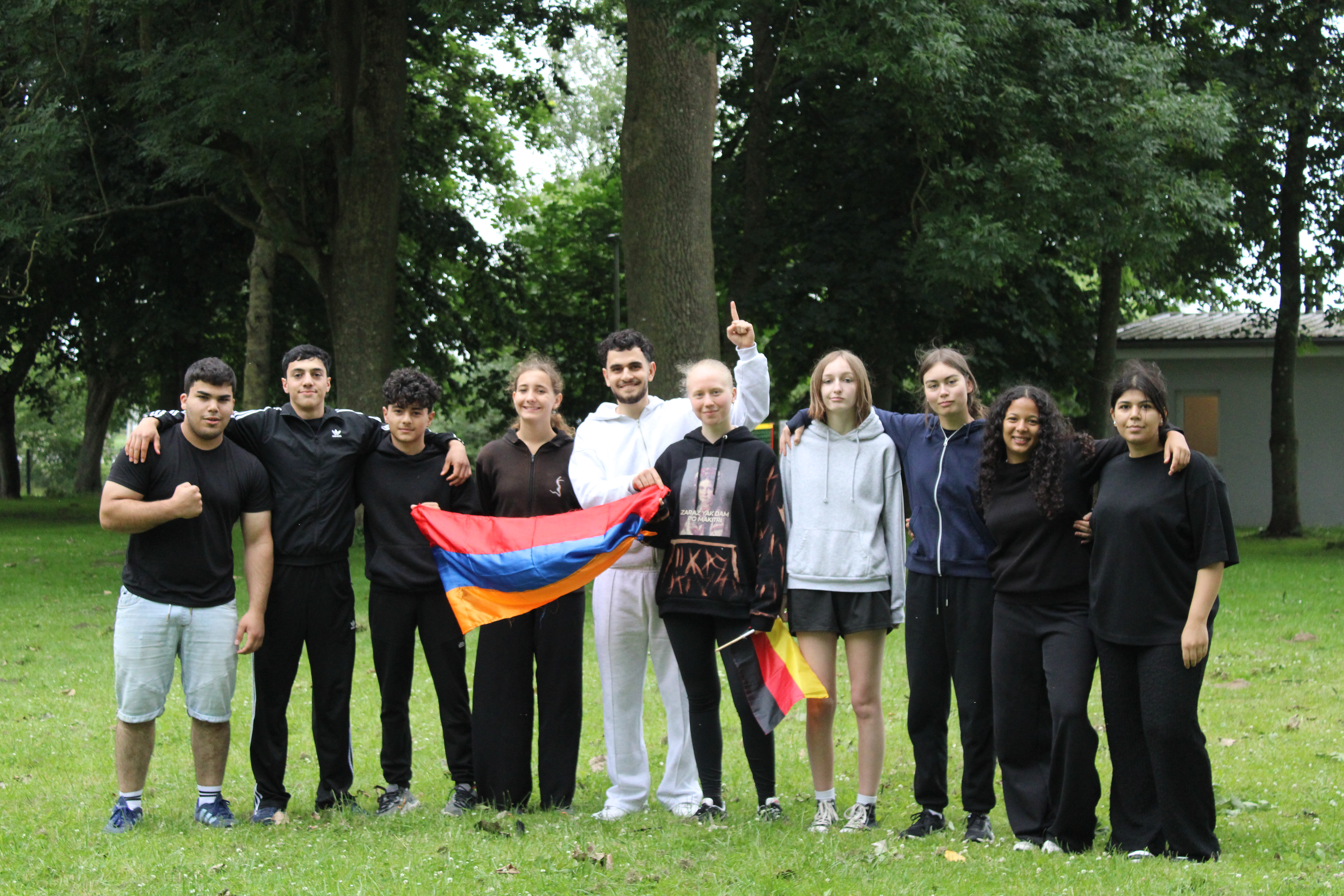 Eine Gruppe junger Menschen steht im Park zusammen, einige halten eine rot-blau-orange Flagge.