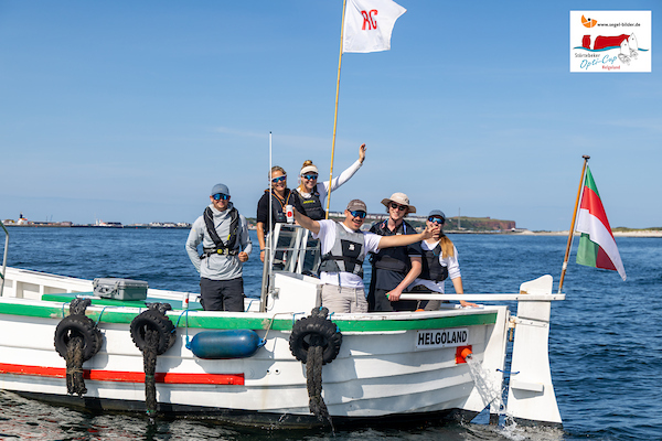 Gruppe von Menschen mit Schwimmwesten auf einem weißen Boot mit grünem Streifen vor offener See.