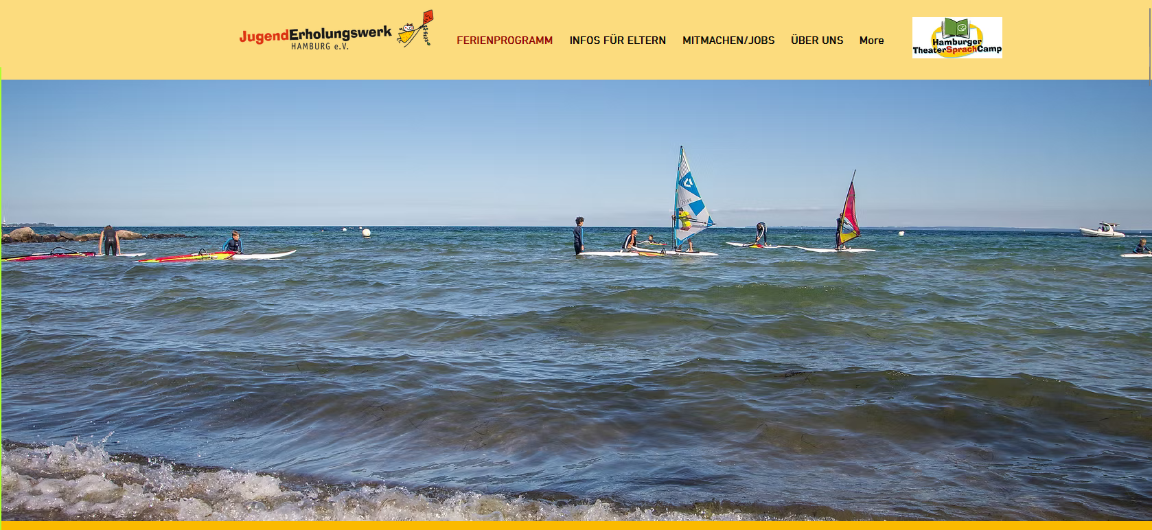 Mehrere Windsurfer auf Brettern gleiten über das blaue Meer unter klarem Himmel.