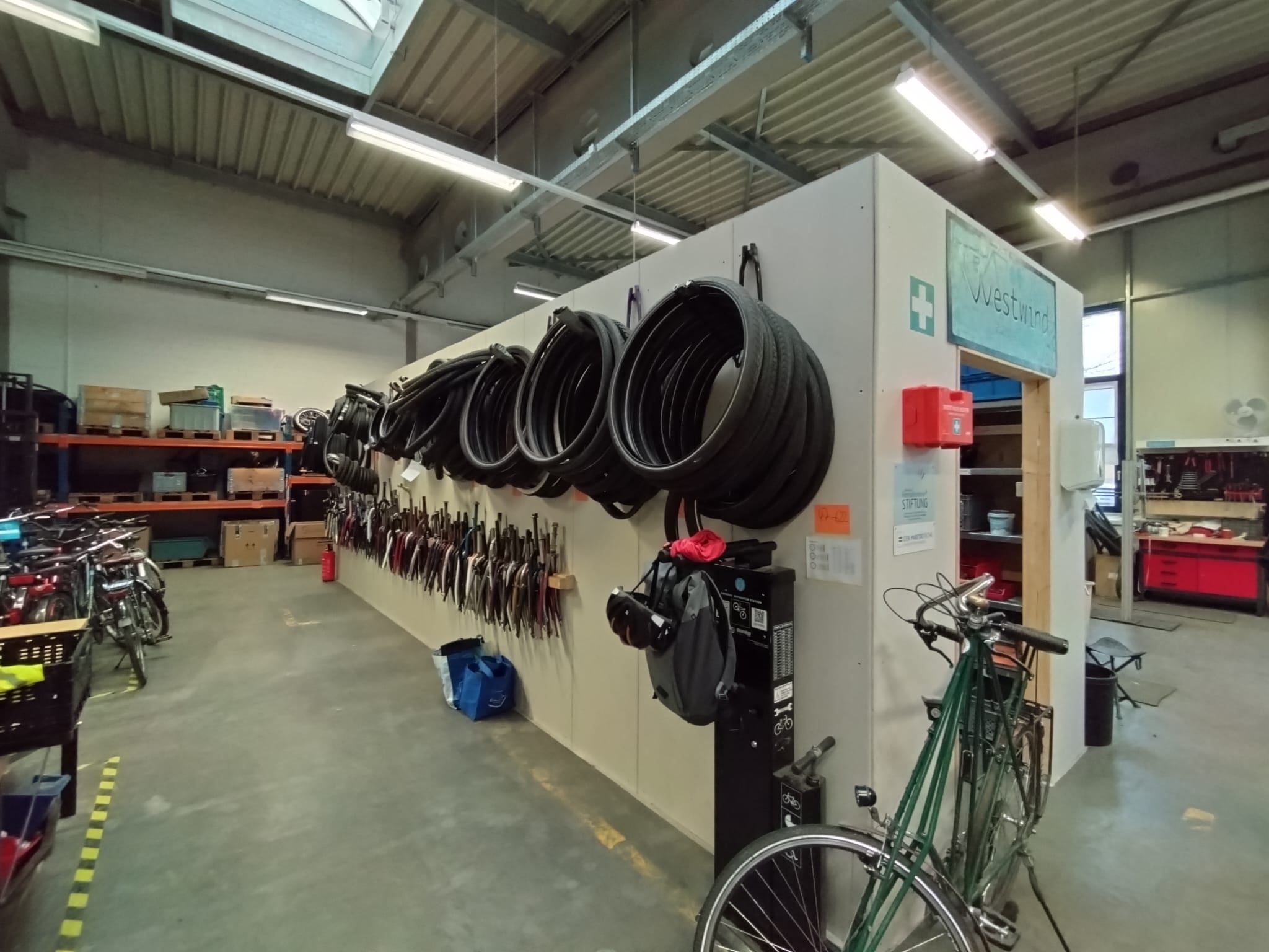 Innenansicht einer Fahrradwerkstatt mit Reifenregalen, zahlreichen Fahrrädern und Werkstattzubehör.