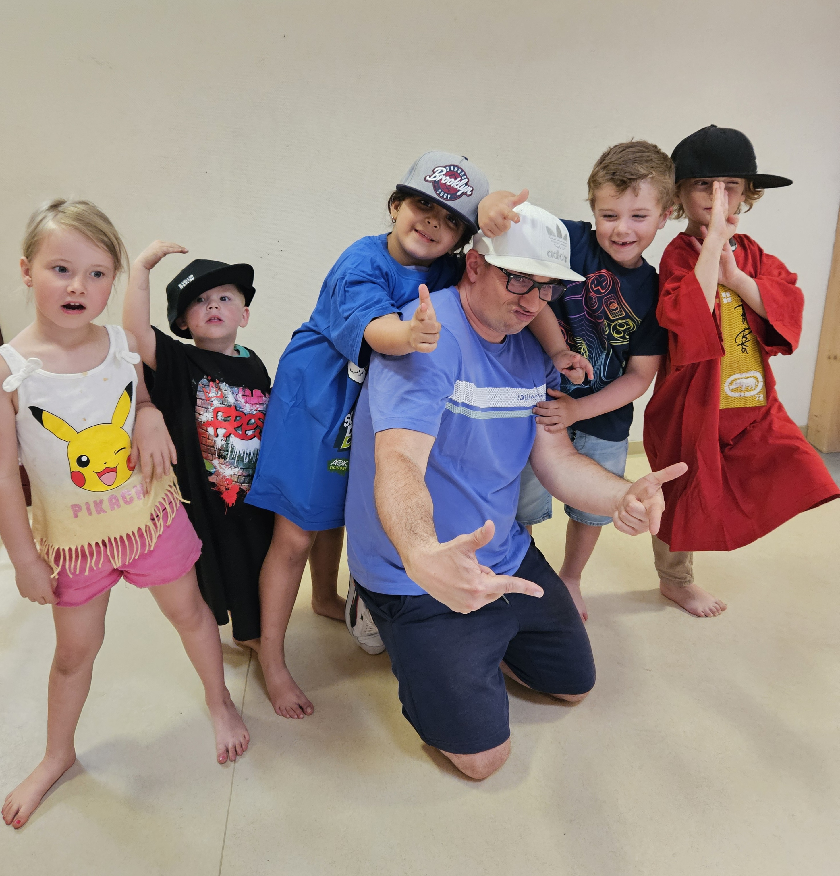 Gruppe fröhlicher Kinder mit einem Erwachsenen posiert zusammen, einige zeigen Peace- oder Daumenzeichen.
