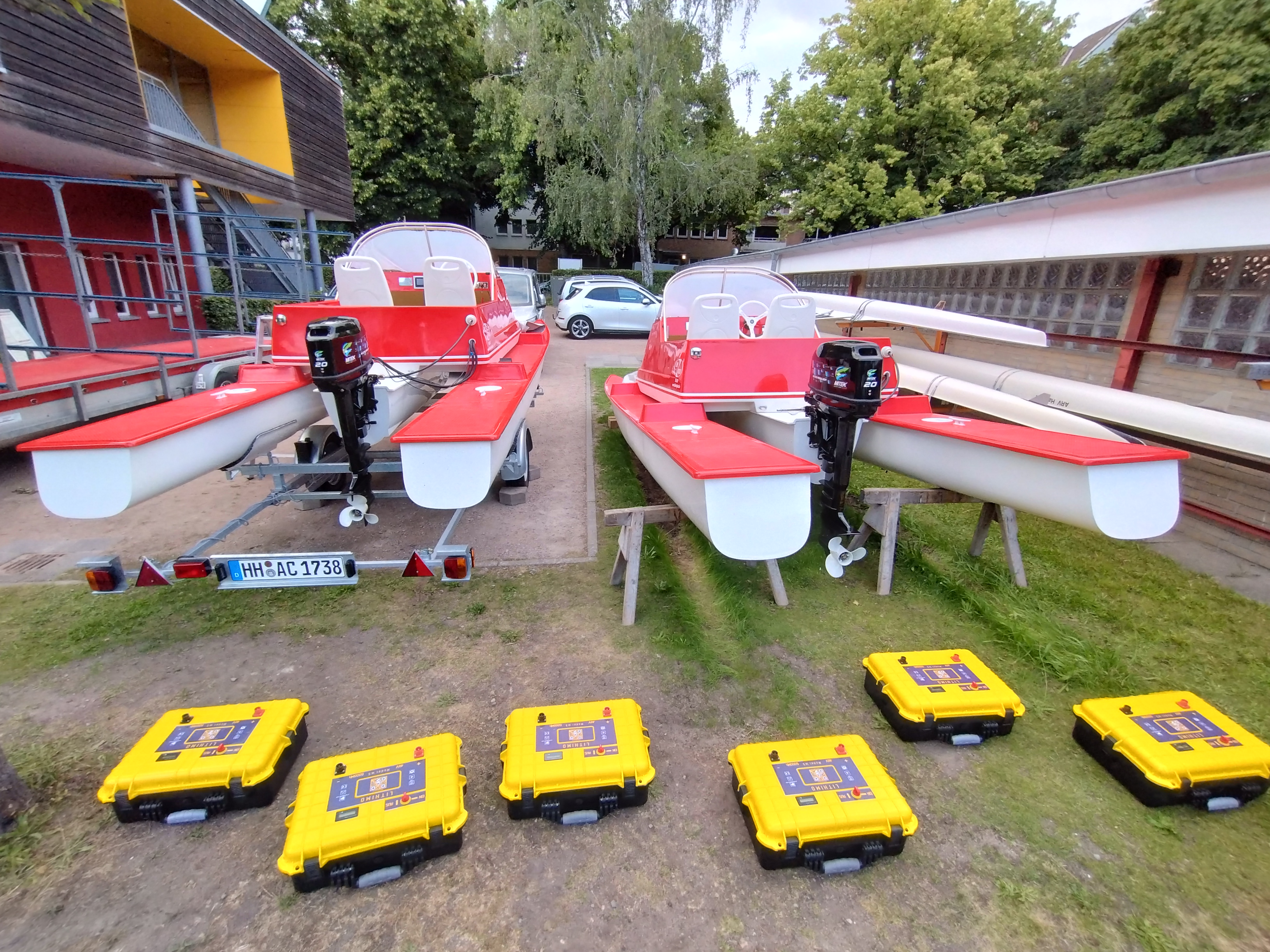 Rote Motorboote mit weißen Sitzen stehen auf Anhängern in einer Außenanlage; gelbe Koffer liegen im Vordergrund.