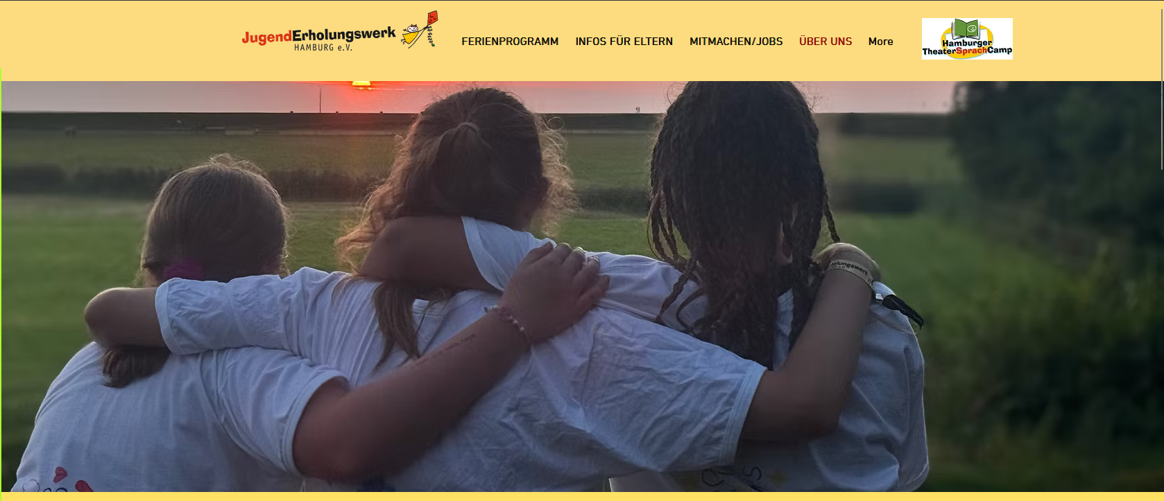 Drei Kinder stehen mit dem Rücken zueinander und umarmen sich auf einer Wiese im Sonnenuntergang.