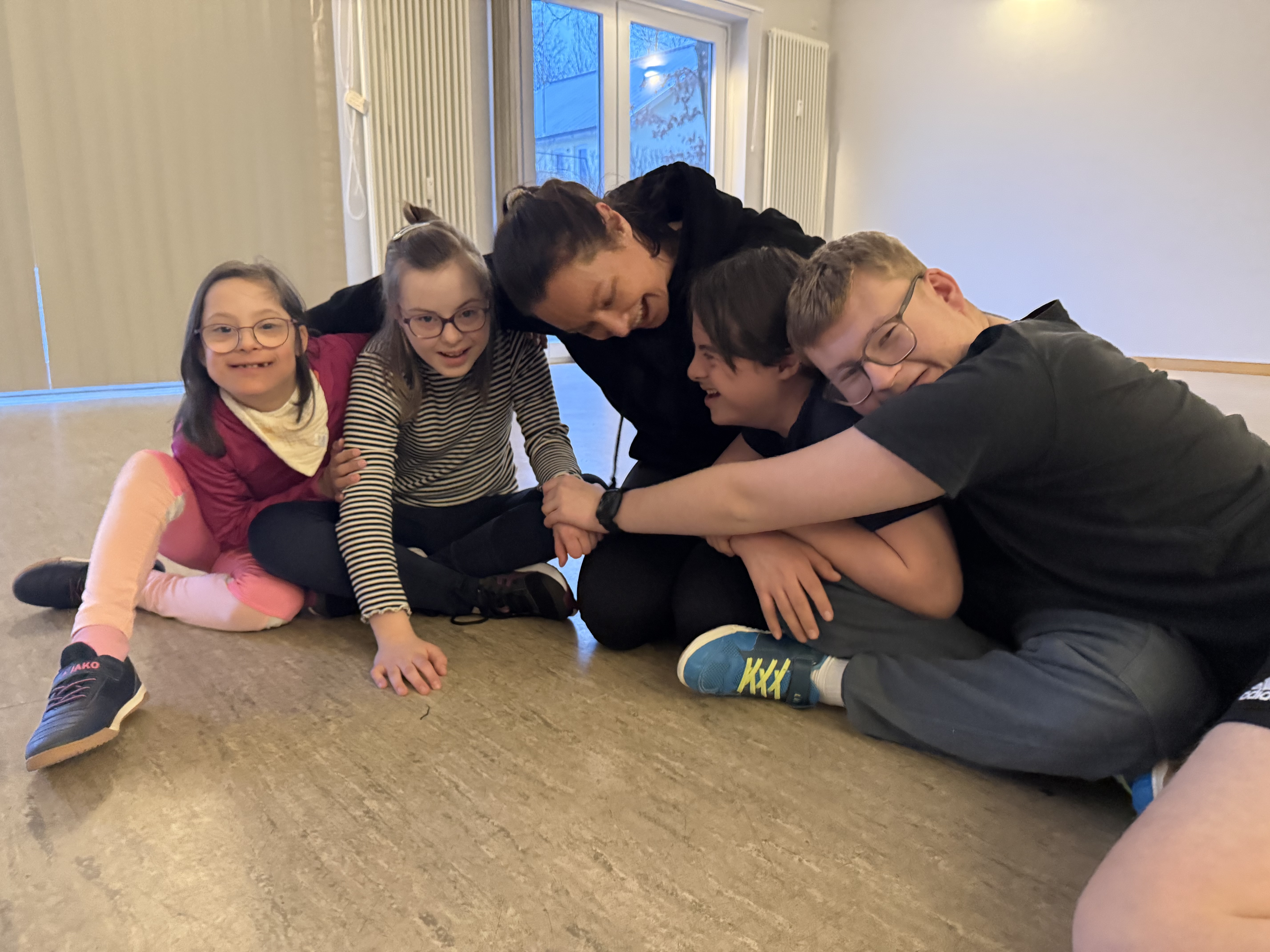 Eine Gruppe junger Menschen sitzt eng auf dem Boden, lacht und umarmt sich.