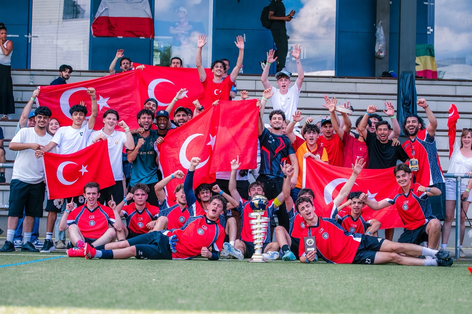 Gruppe junger Sportler feiert auf der Tribüne mit türkischen Flaggen und Pokal.