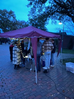 Gruppe von Personen steht unter einem burgunderfarbenen Pavillon mit Lichterketten auf gepflastertem Platz bei Abenddämmerung
