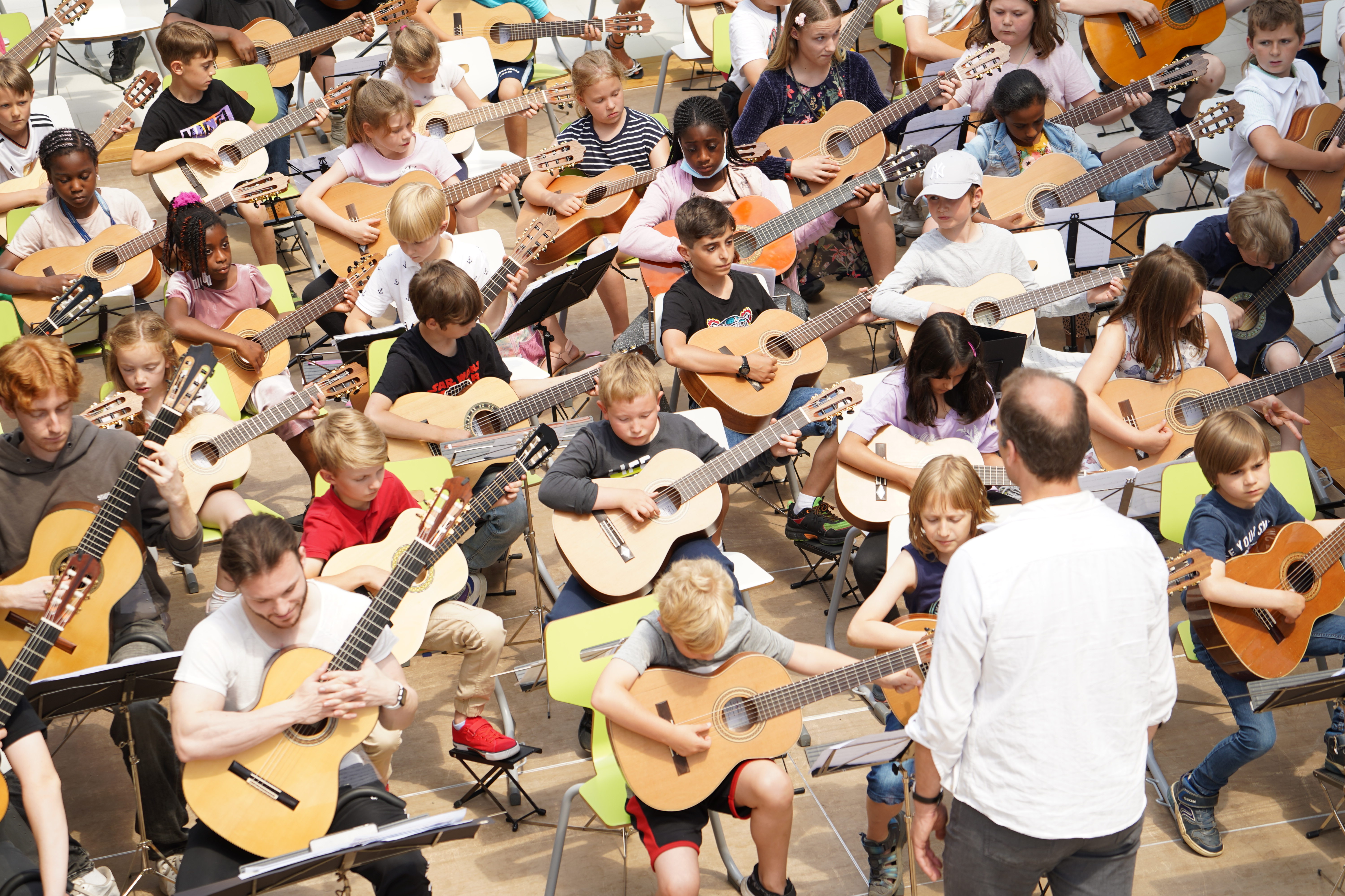 Viele Kinder spielen gemeinsam Gitarren in einer großen Gruppe beim Musikunterricht.