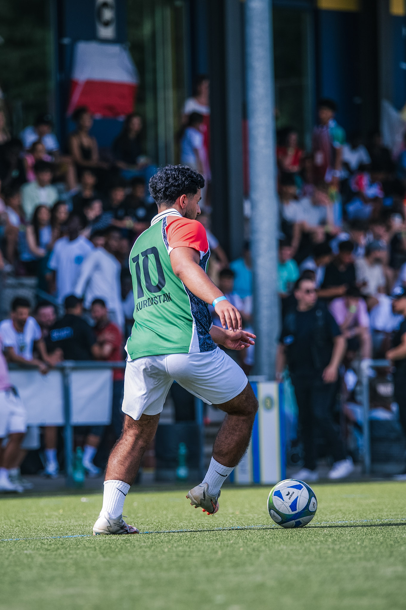 Fußballspieler in grünem Trikot (Nr. 10) mit Ball am Fuß, vor jubelnder Zuschauermenge.